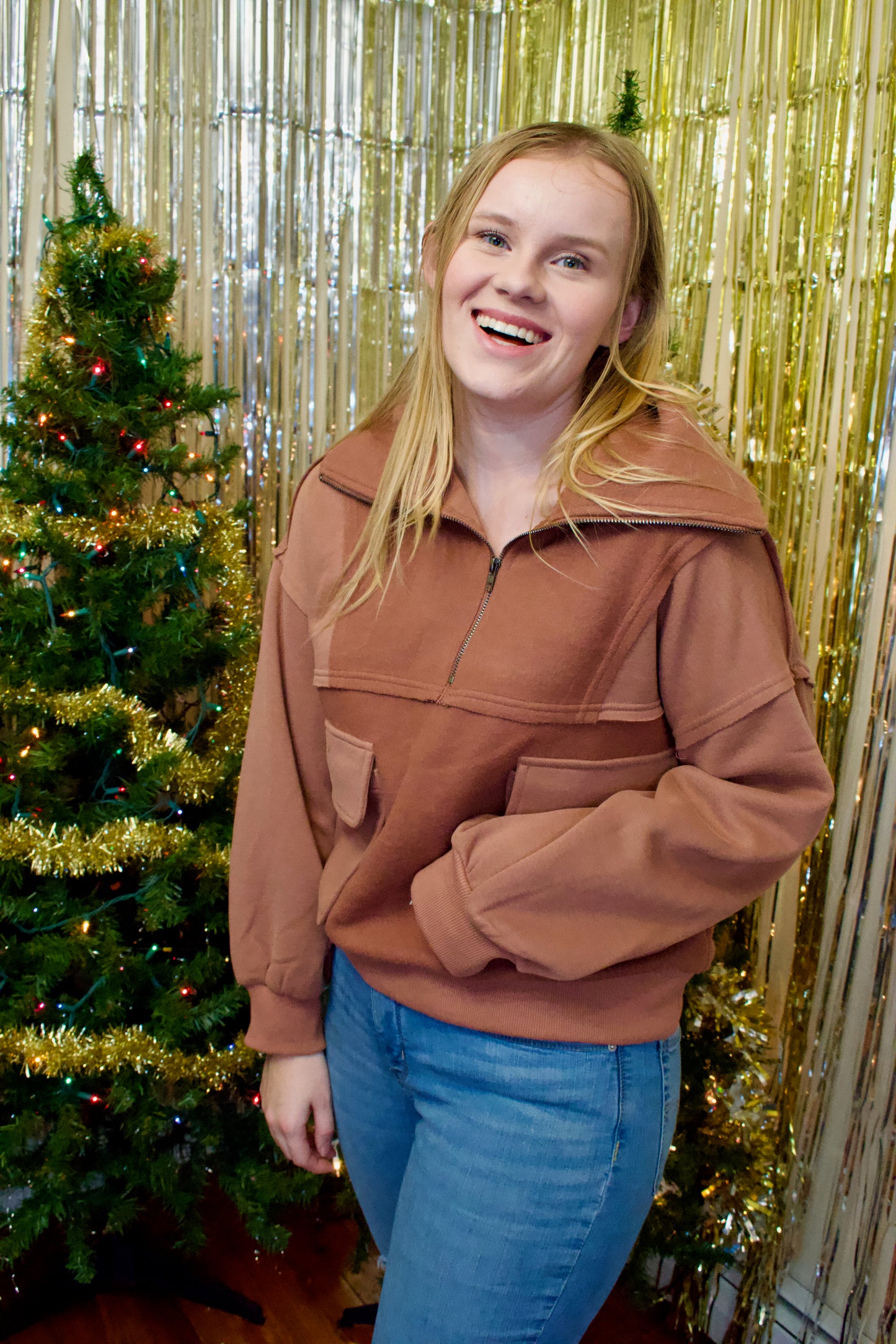 A woman wearing a bown half zip top, with two large kangaroo pockets on the front