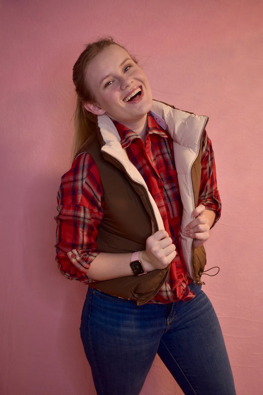 A woman wearing a reversible puffer vest. The vest is brown on one side and beige on the other. The brown side is facing outwards