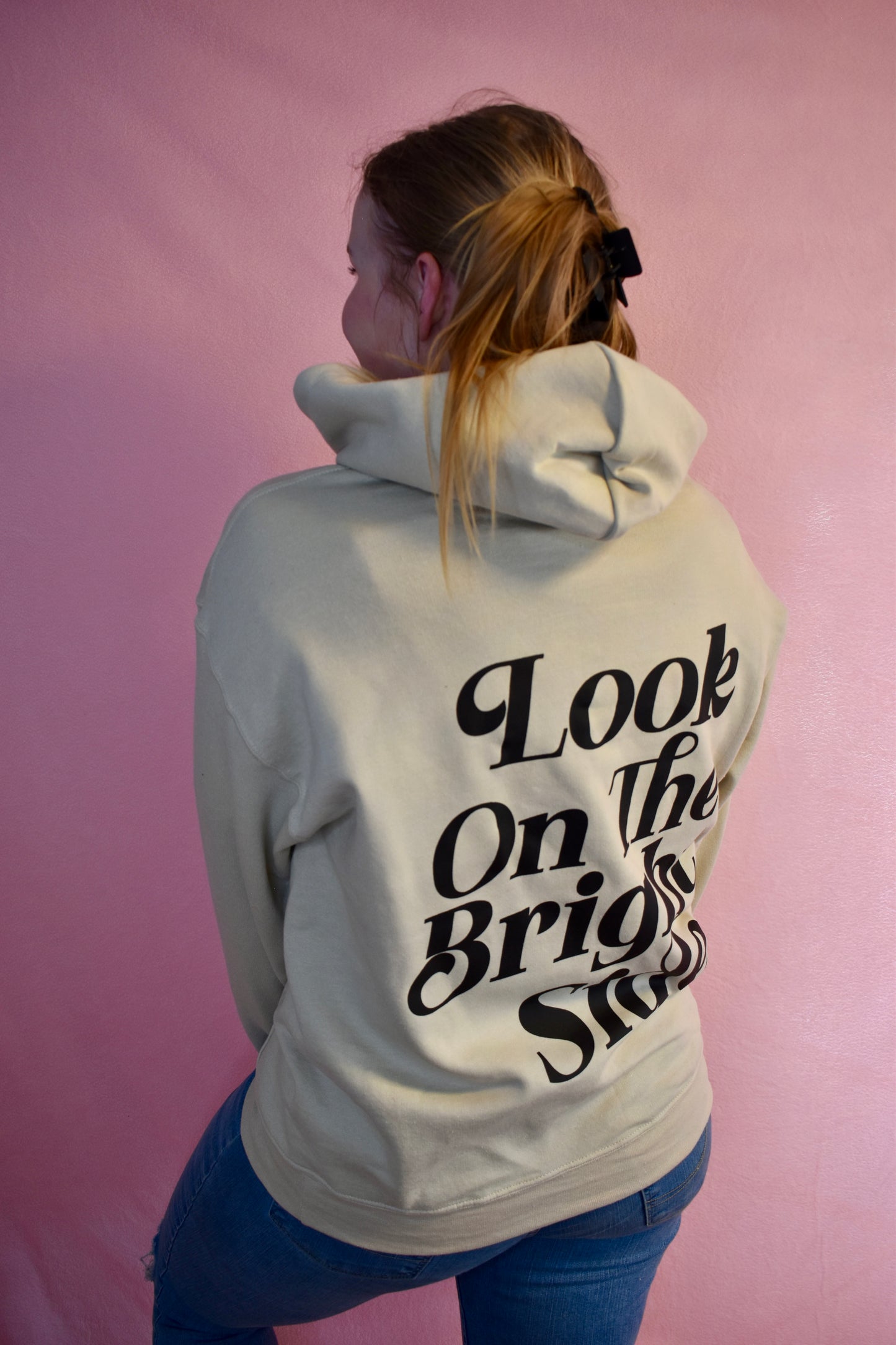 Woman wearing a beige hoodie printed with the words Look On The Bright Side