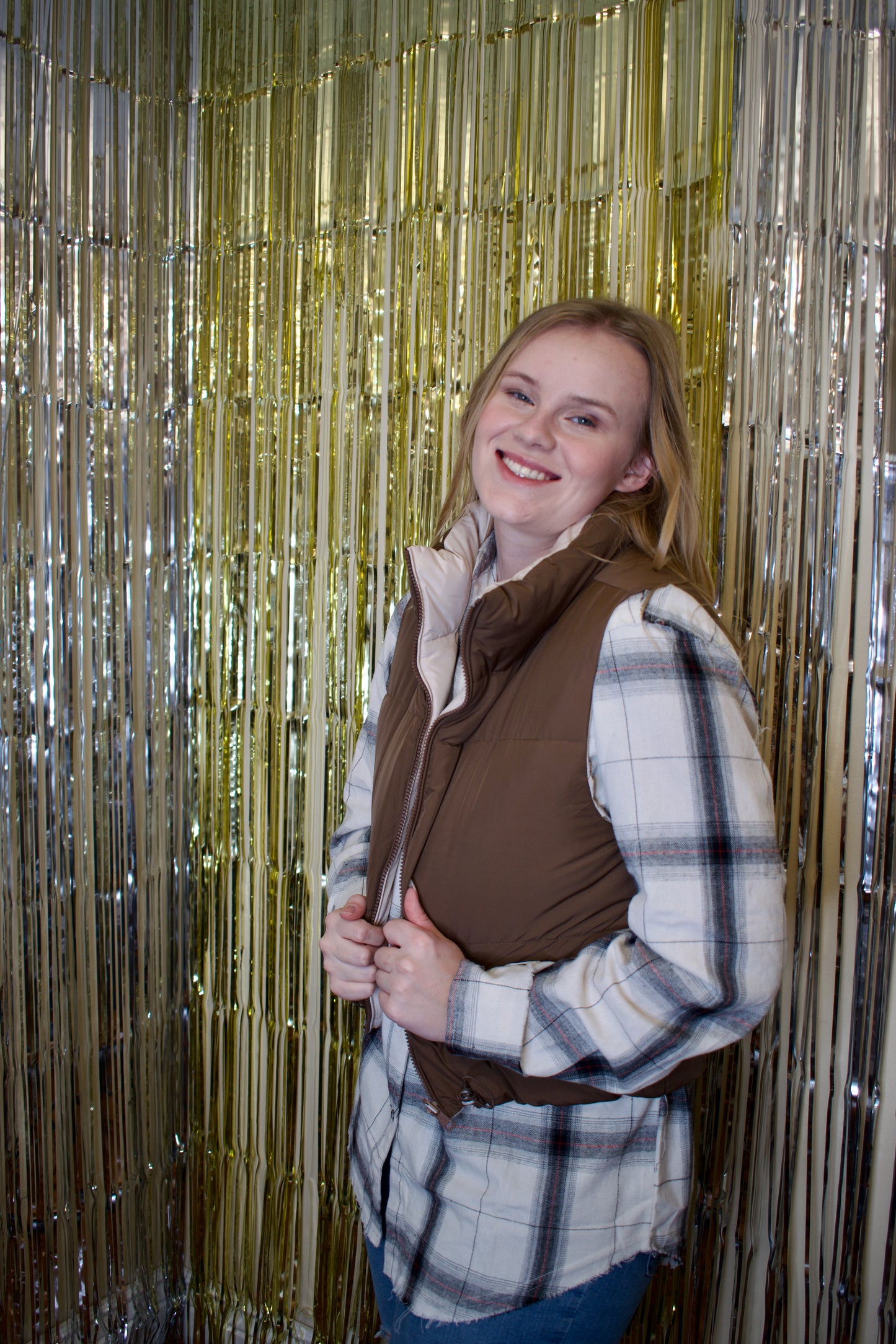 A woman wearing a reversible puffer vest. The vest is brown on one side and beige on the other. The brown side is facing outwards