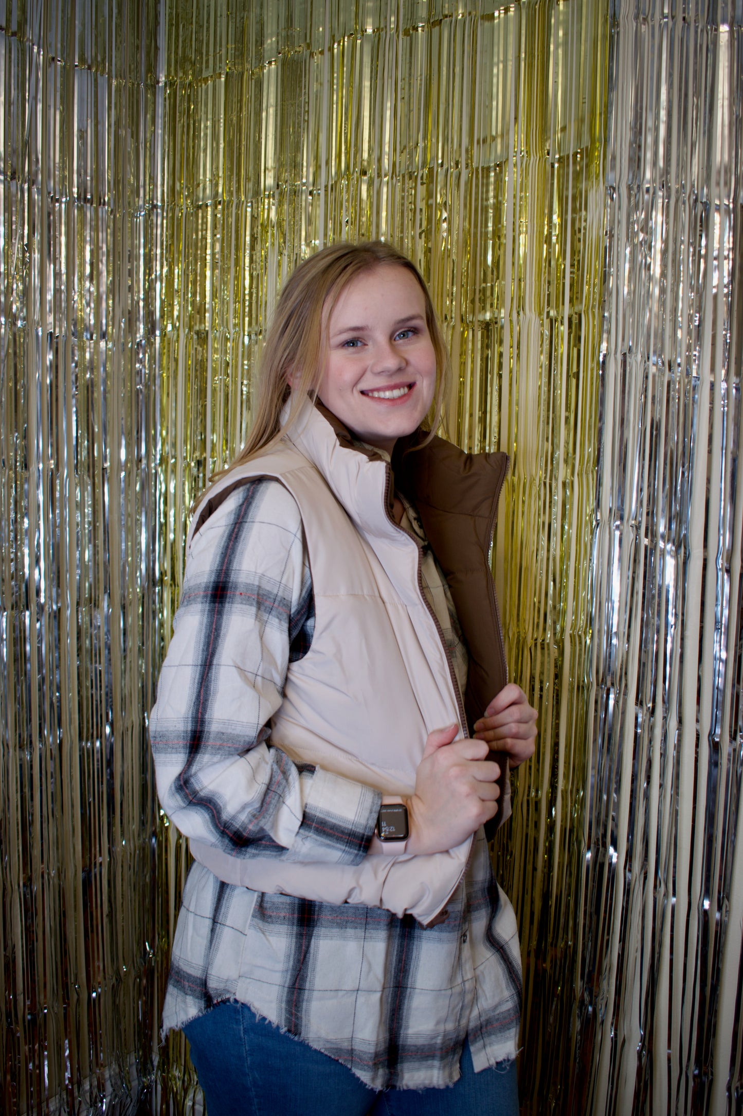 A woman wearing a reversible puffer vest. The vest is brown on one side and beige on the other. The beige side is facing outwards