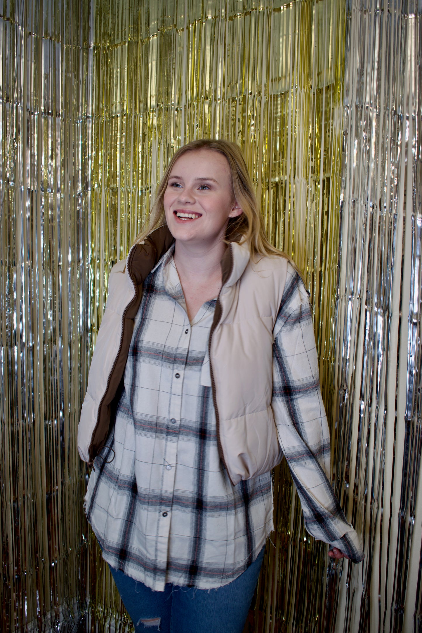 A woman wearing a reversible puffer vest. The vest is brown on one side and beige on the other. The beige side is facing outwards