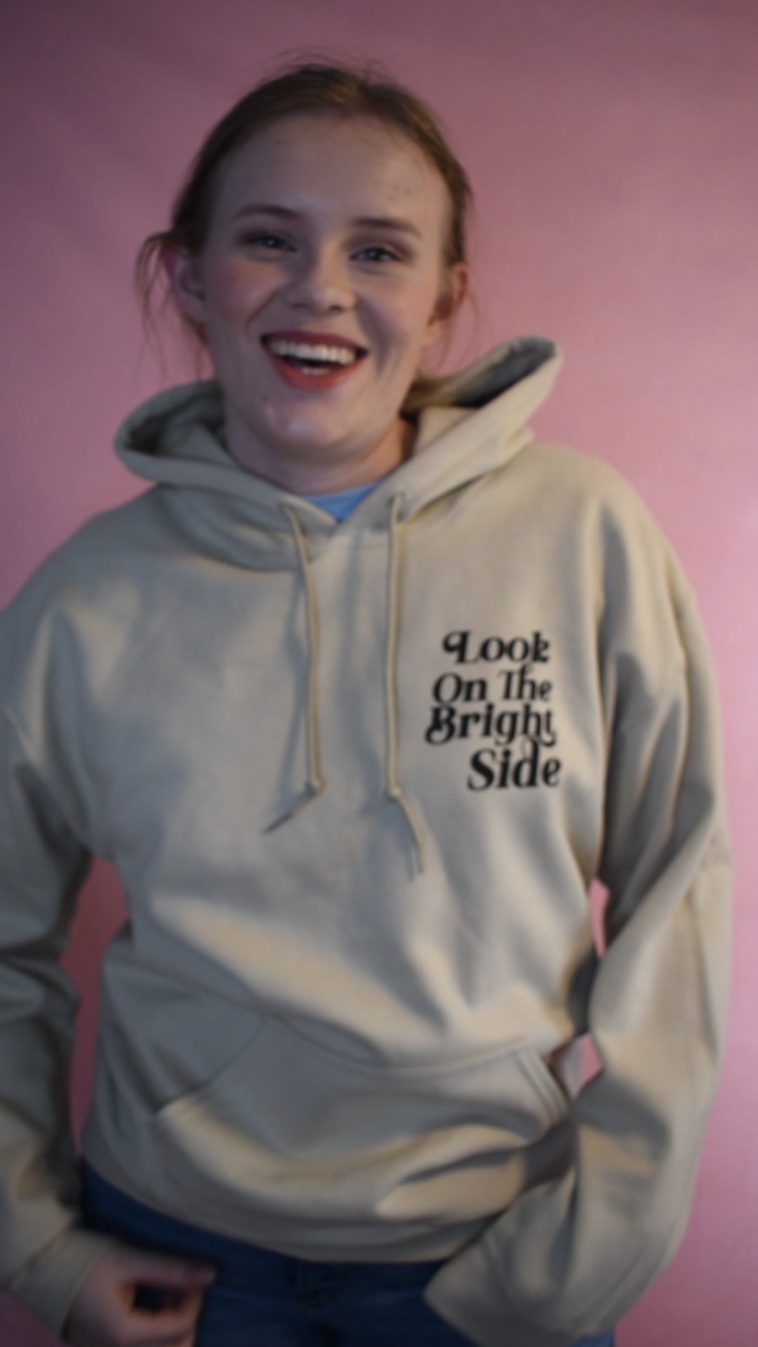 Woman wearing a beige hoodie printed with the words Look On The Bright Side. She is talking about why she likes it