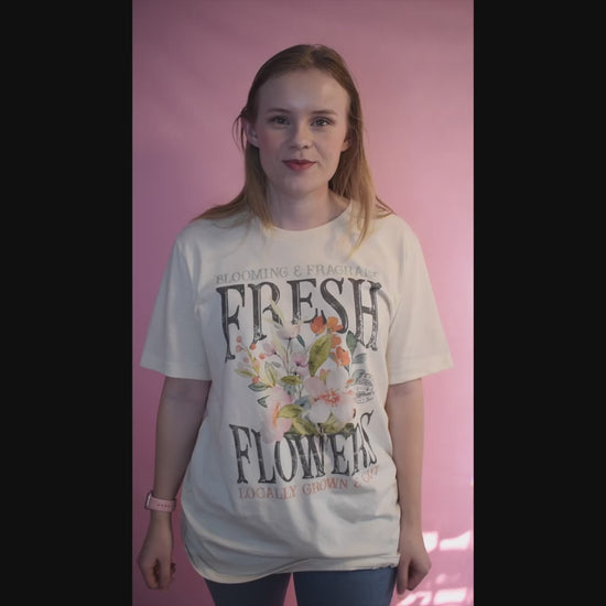 Short Video of a woman wearing a beige tee with a fresh flowers design on it. She is explaining how it is oversized and perfect for spring